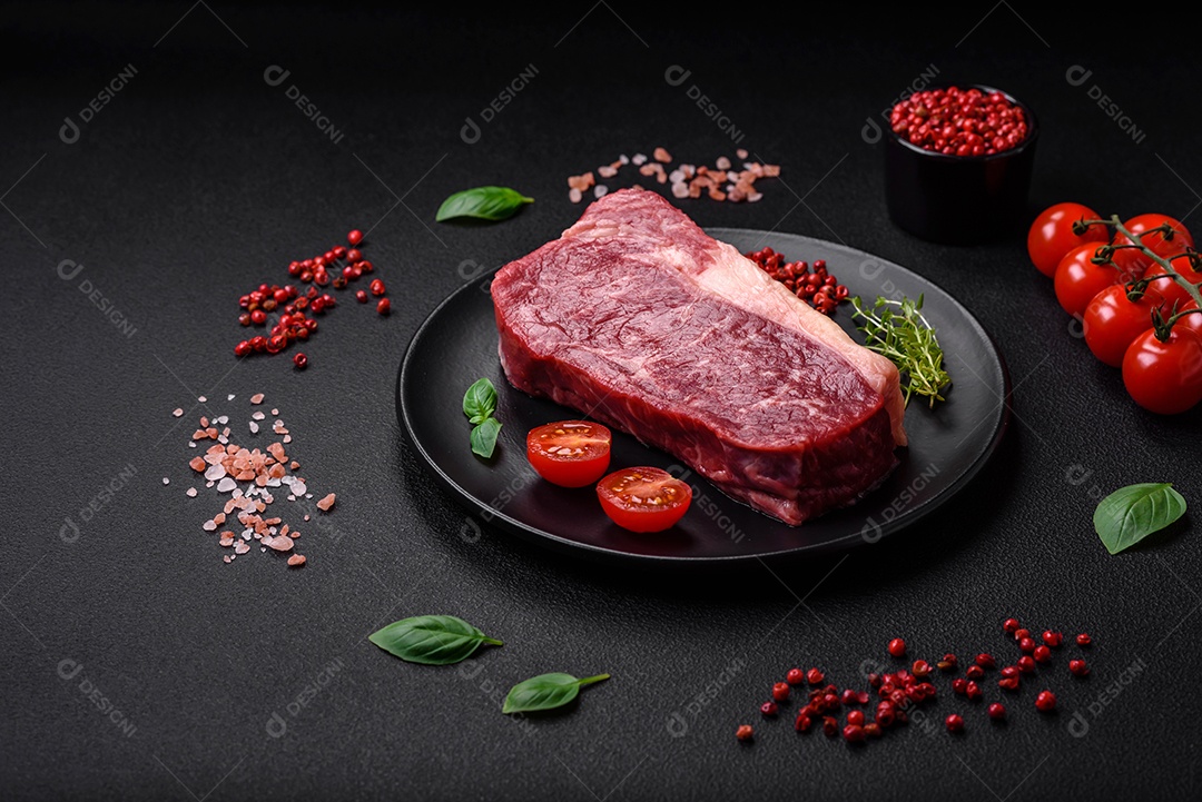 Bife de carne crua fresca com sal, especiarias e ervas sobre um fundo escuro de concreto