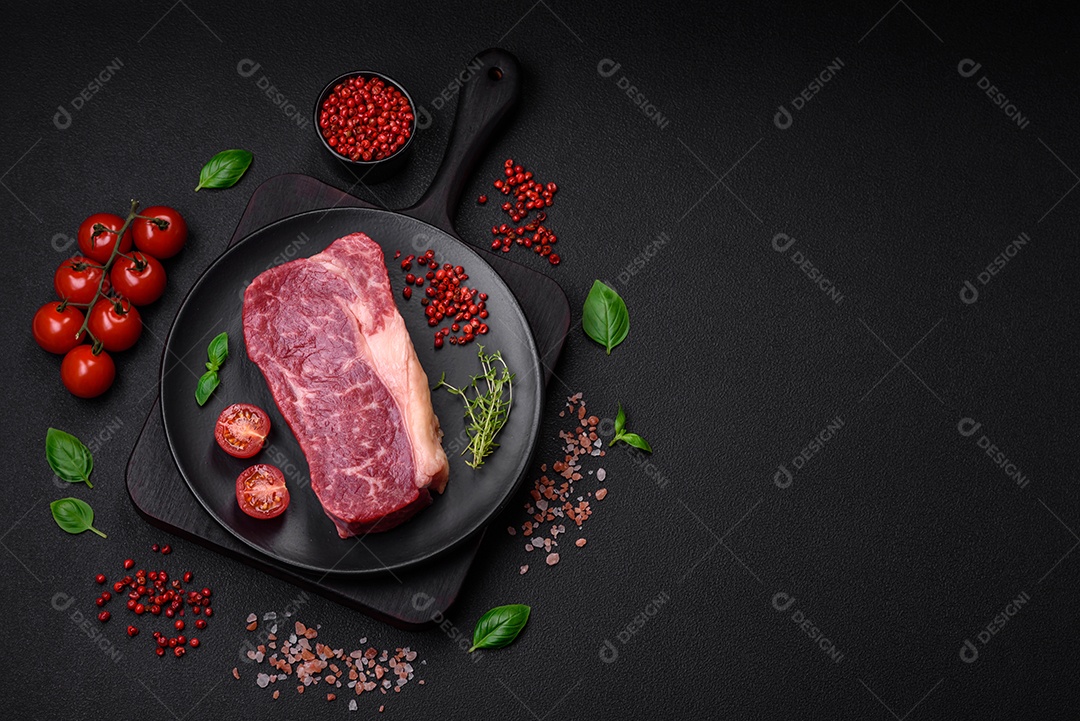 Bife de carne crua fresca com sal, especiarias e ervas sobre um fundo escuro de concreto