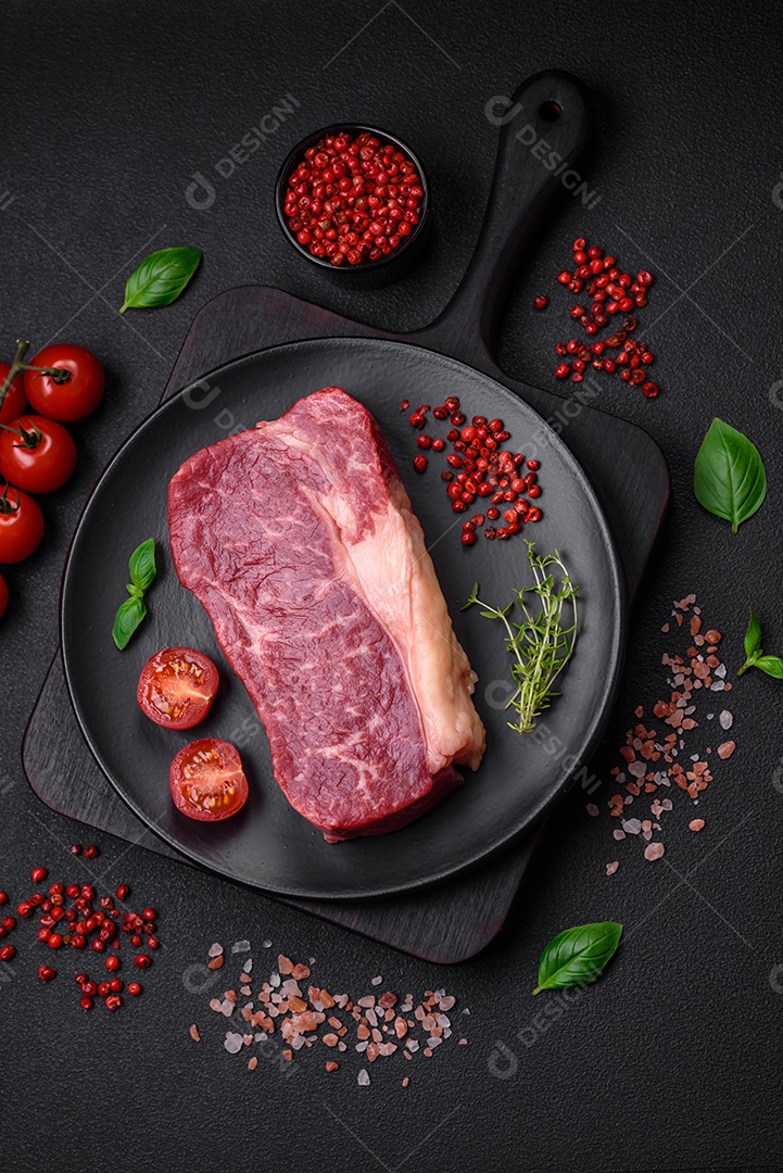 Bife de carne crua fresca com sal, especiarias e ervas sobre um fundo escuro de concreto
