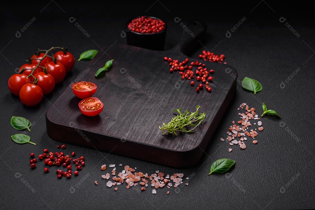 Ingredientes para cozinhar tomate cereja, sal, especiarias e ervas sobre um fundo escuro de concreto