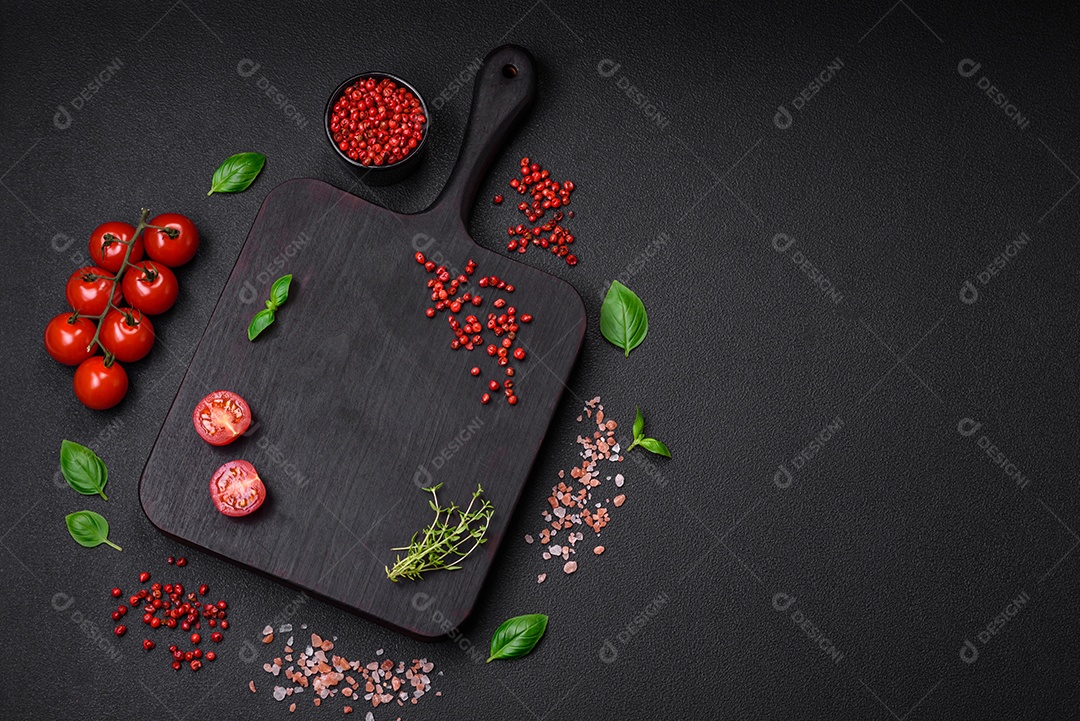 Ingredientes para cozinhar tomate cereja, sal, especiarias e ervas sobre um fundo escuro de concreto