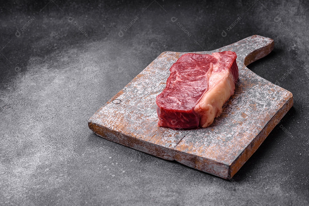 Bife de carne crua fresca com sal, especiarias e ervas sobre um fundo escuro de concreto
