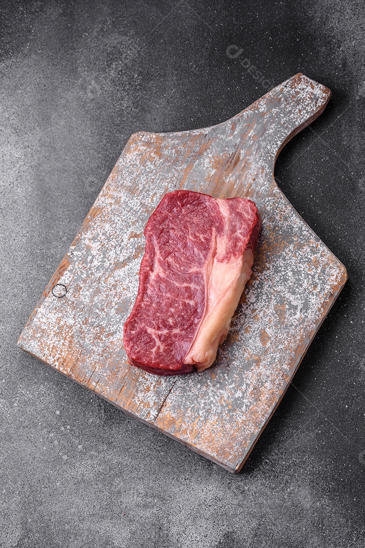Bife de carne crua fresca com sal, especiarias e ervas sobre um fundo escuro de concreto