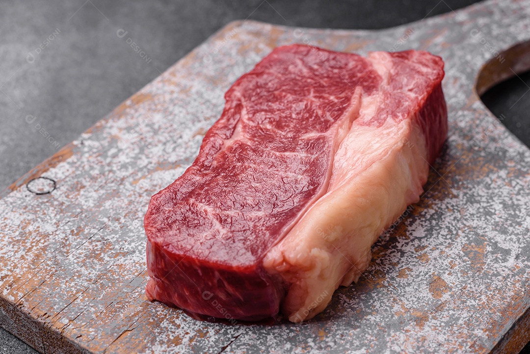 Bife de carne crua fresca com sal, especiarias e ervas sobre um fundo escuro de concreto