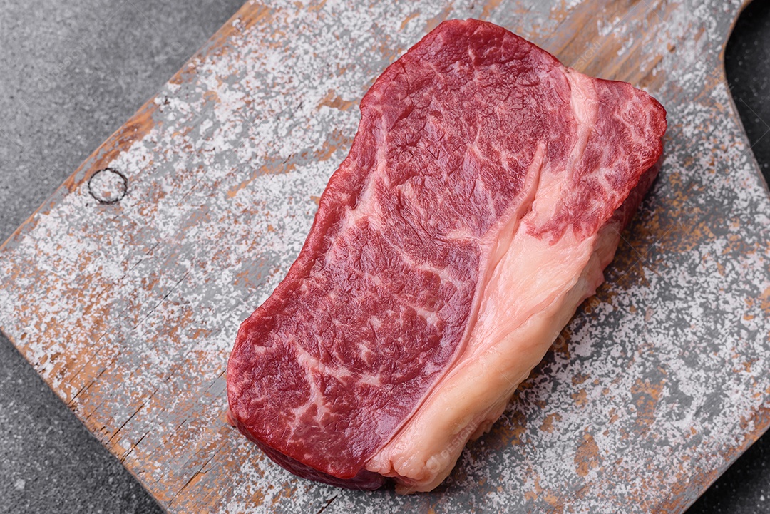 Bife de carne crua fresca com sal, especiarias e ervas sobre um fundo escuro de concreto