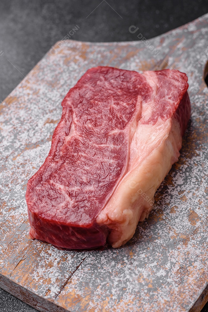 Bife de carne crua fresca com sal, especiarias e ervas sobre um fundo escuro de concreto