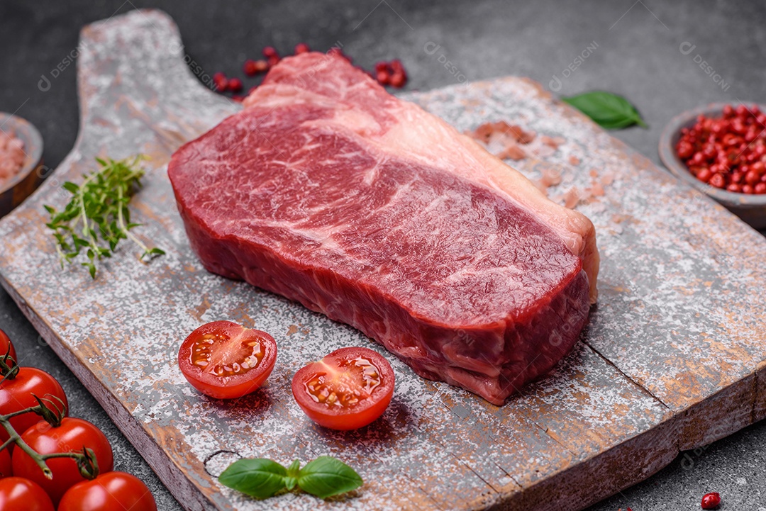 Bife de carne crua fresca com sal, especiarias e ervas sobre um fundo escuro de concreto