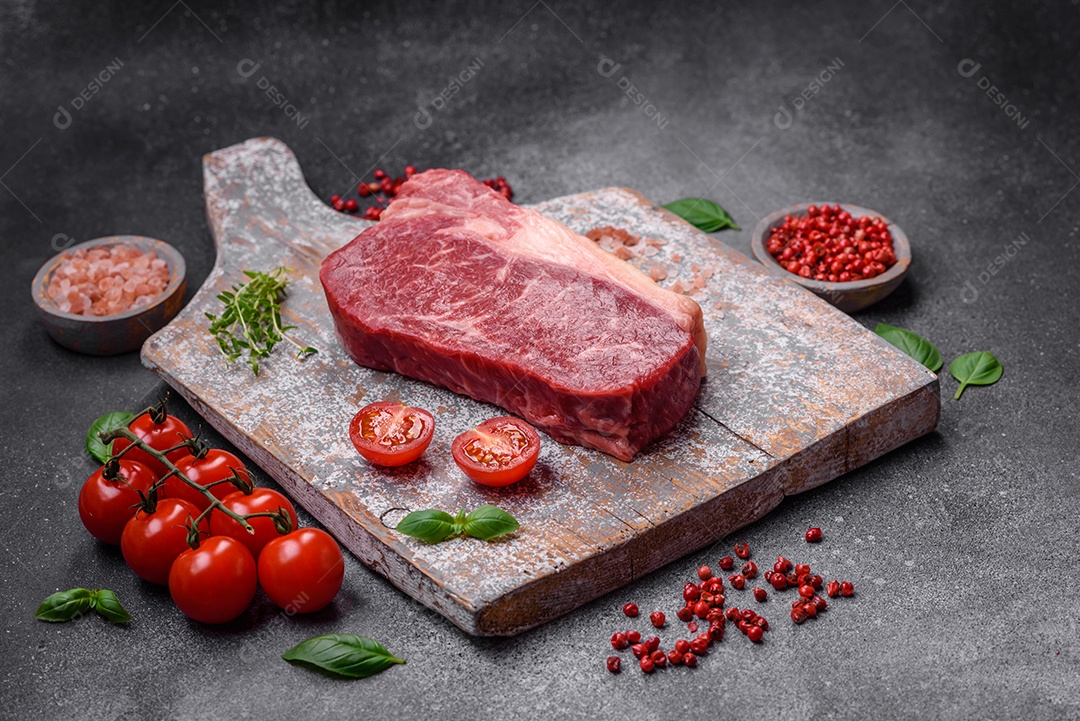 Bife de carne crua fresca com sal, especiarias e ervas sobre um fundo escuro de concreto