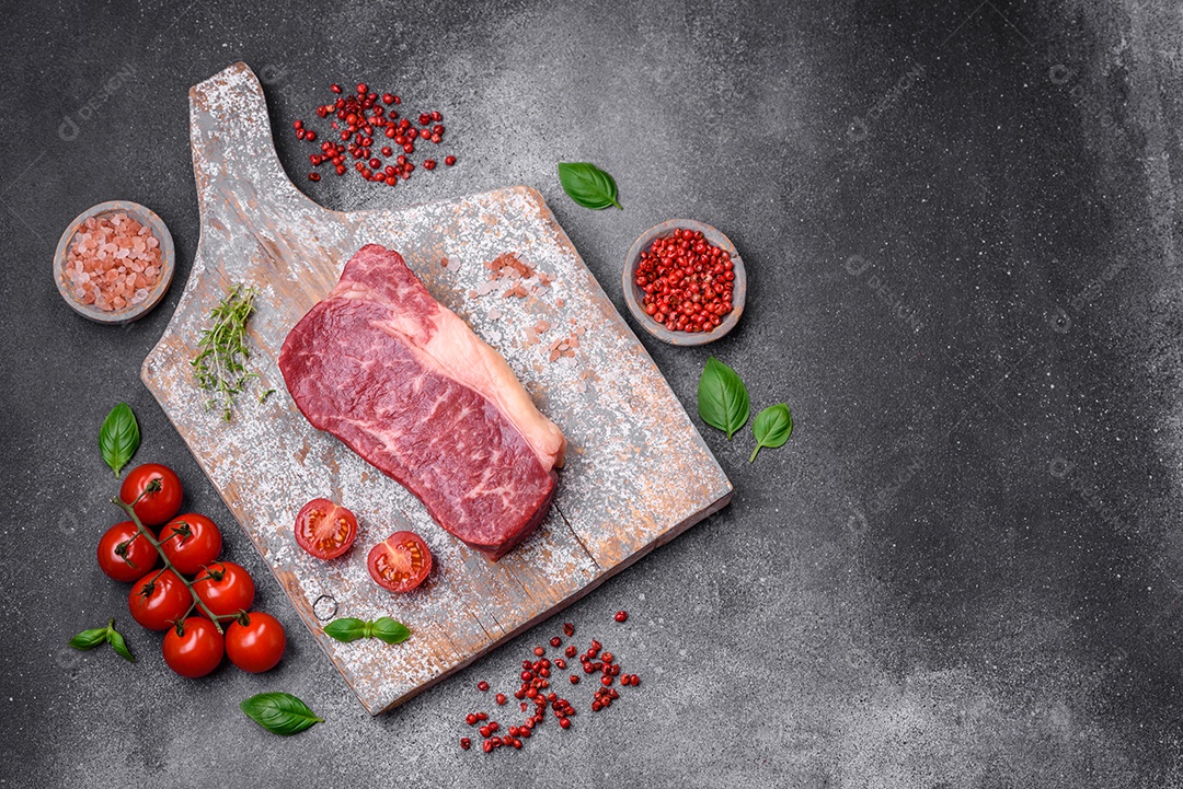 Bife de carne crua fresca com sal, especiarias e ervas sobre um fundo escuro de concreto