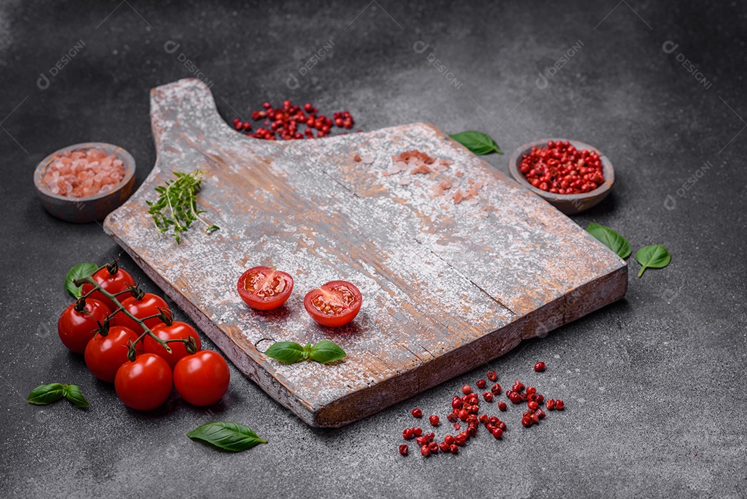 Ingredientes para cozinhar tomate cereja, sal, especiarias e ervas sobre um fundo escuro de concreto