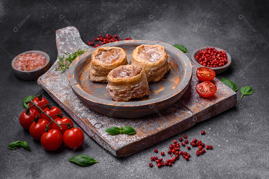 Deliciosos rolos de carne de porco ou frango crus e frescos embrulhados em bacon, com sal, especiarias e ervas sobre um fundo escuro de concreto