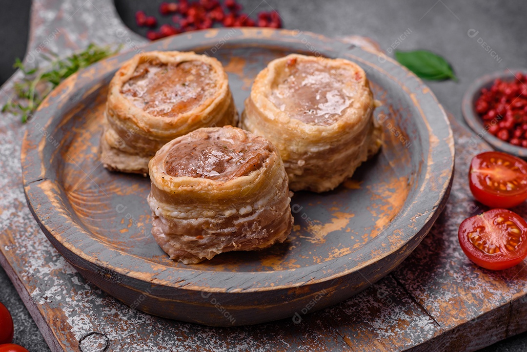 Deliciosos rolos de carne de porco ou frango crus e frescos embrulhados em bacon, com sal, especiarias e ervas sobre um fundo escuro de concreto