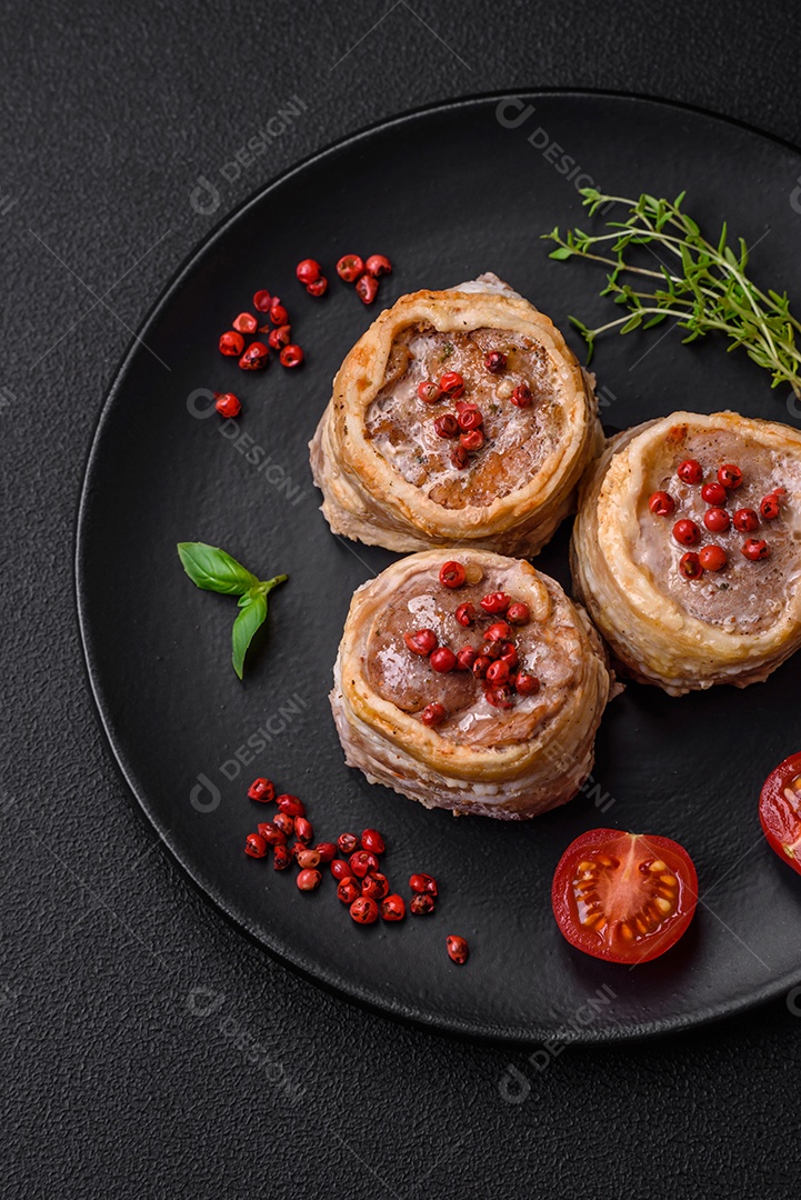 Deliciosos rolos de carne de porco ou frango crus e frescos embrulhados em bacon, com sal, especiarias e ervas sobre um fundo escuro de concreto