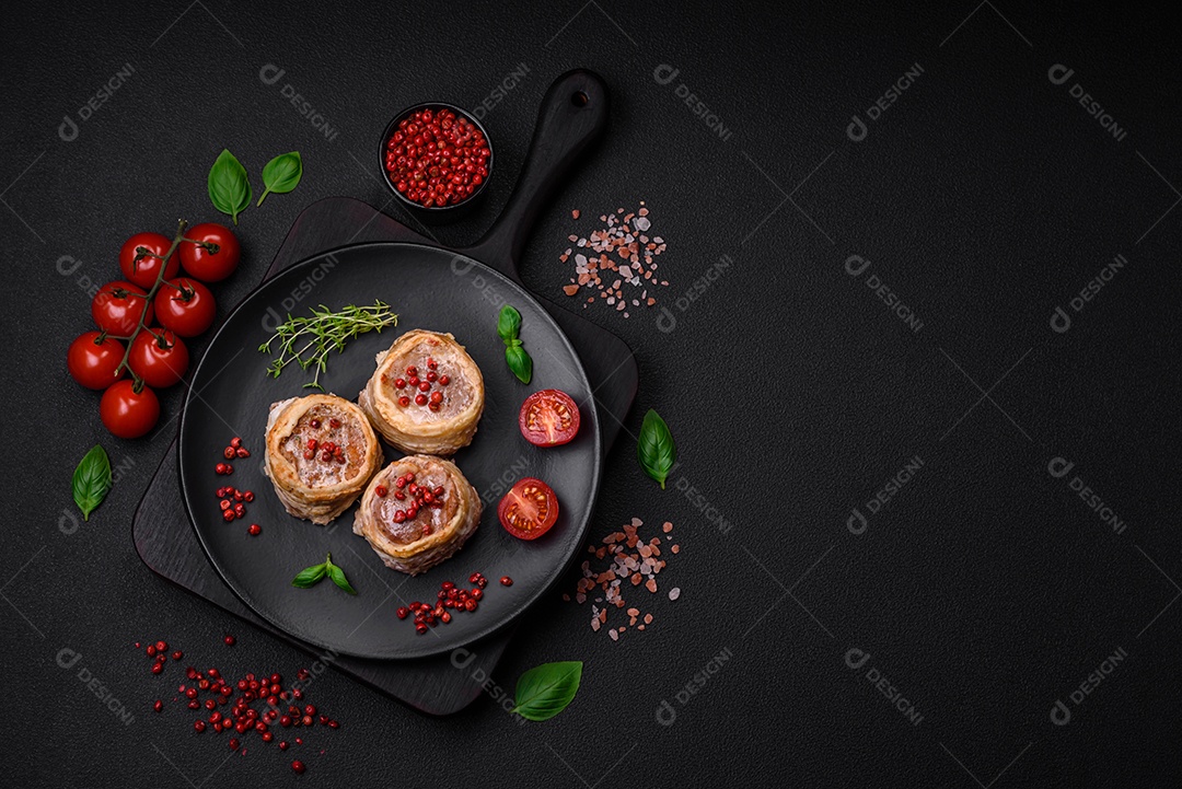 Deliciosos rolos de carne de porco ou frango crus e frescos embrulhados em bacon, com sal, especiarias e ervas sobre um fundo escuro de concreto