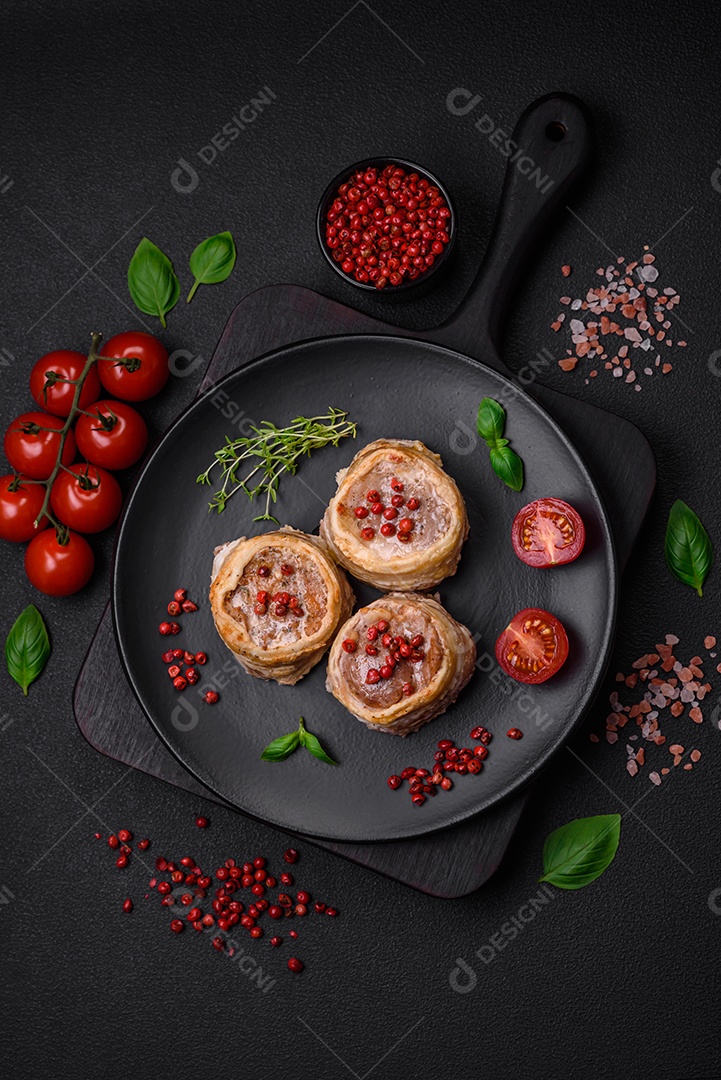 Deliciosos rolos de carne de porco ou frango crus e frescos embrulhados em bacon, com sal, especiarias e ervas sobre um fundo escuro de concreto