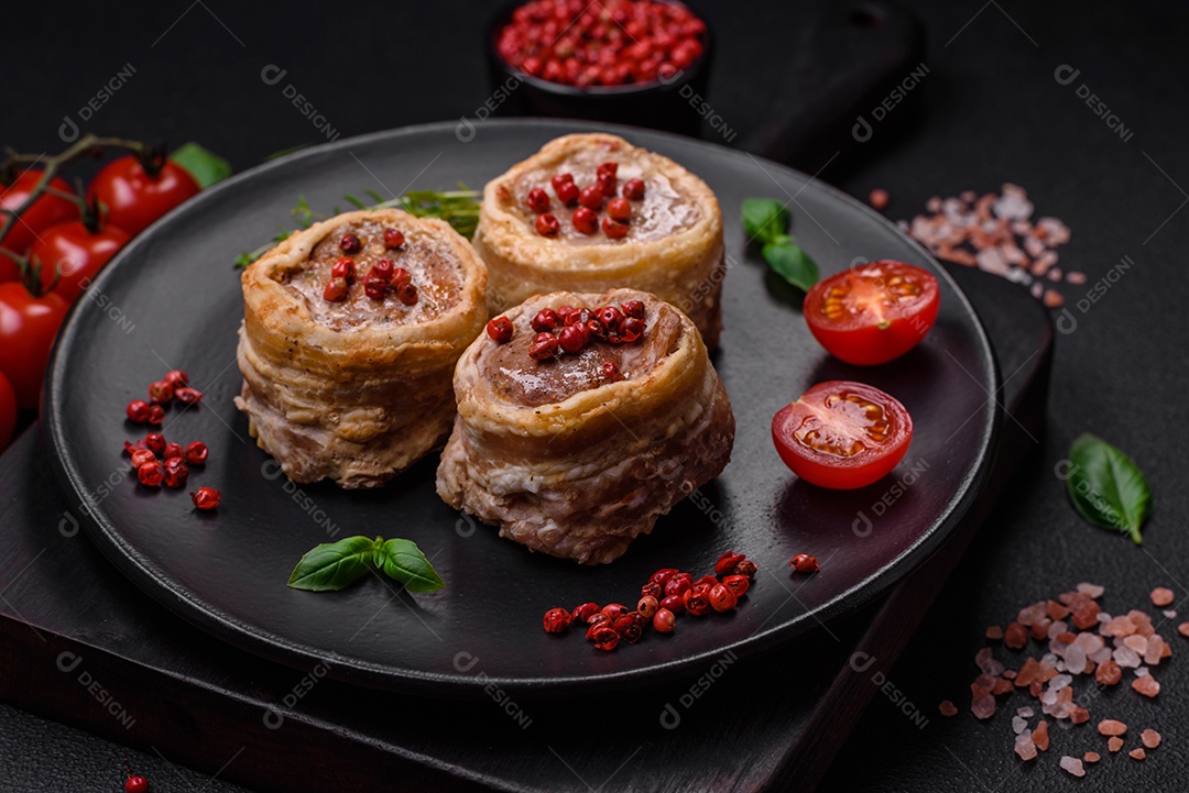 Deliciosos rolos de carne de porco ou frango crus e frescos embrulhados em bacon, com sal, especiarias e ervas sobre um fundo escuro de concreto