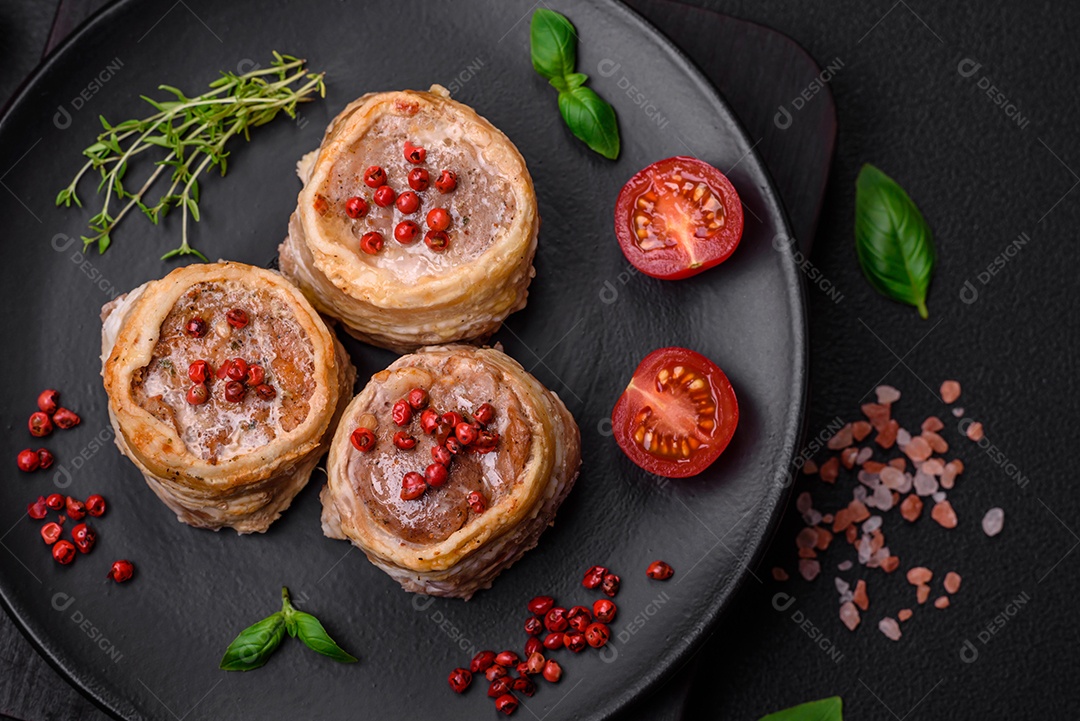 Deliciosos rolos de carne de porco ou frango crus e frescos embrulhados em bacon, com sal, especiarias e ervas sobre um fundo escuro de concreto