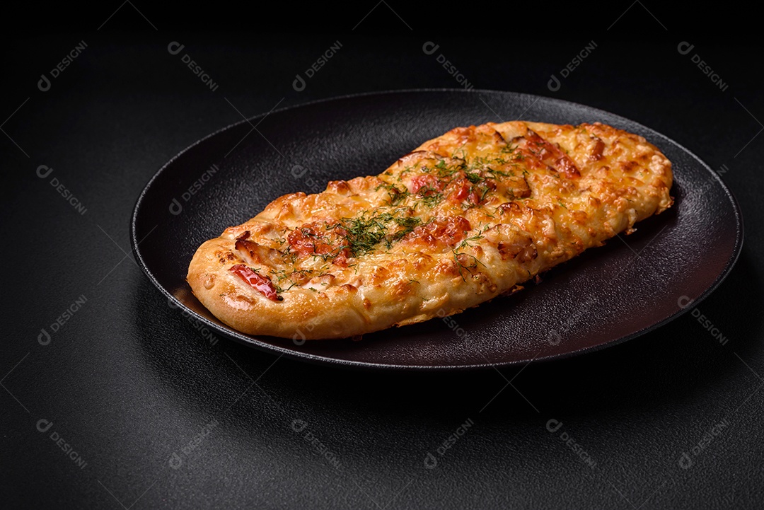 Deliciosa pizza de pão achatado fresco com queijo, tomate, salsicha, sal e especiarias sobre um fundo escuro de concreto