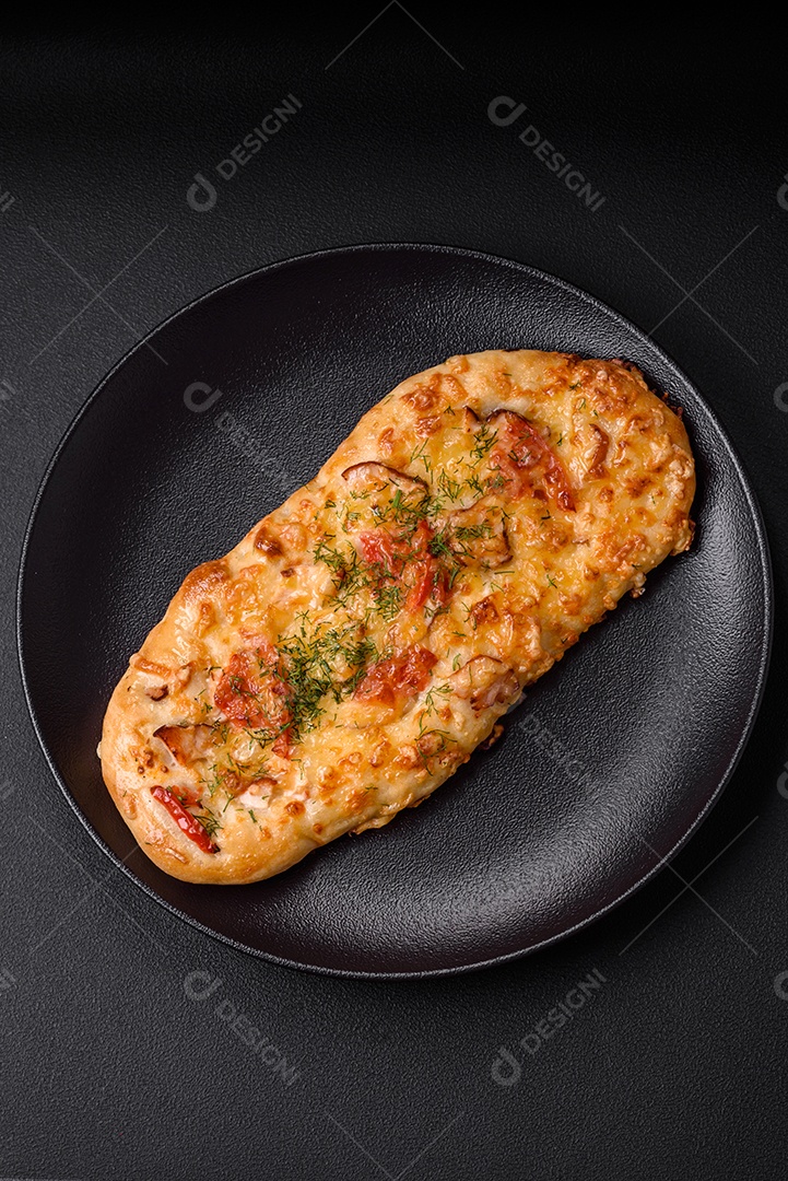 Deliciosa pizza de pão achatado fresco com queijo, tomate, salsicha, sal e especiarias sobre um fundo escuro de concreto