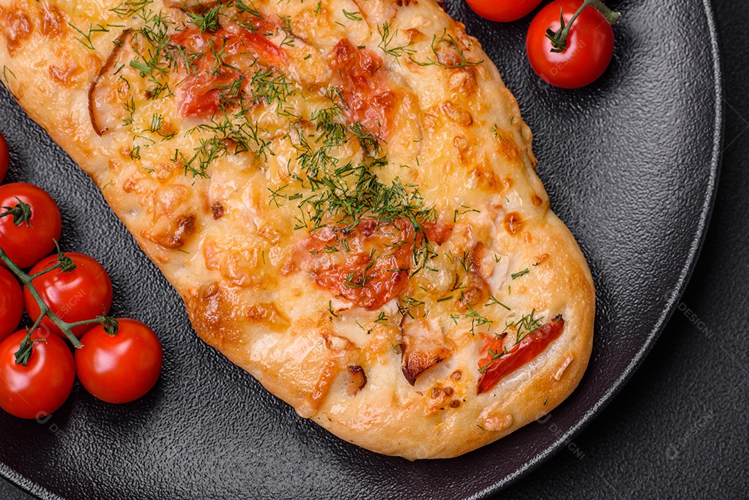 Deliciosa pizza de pão achatado fresco com queijo, tomate, salsicha, sal e especiarias sobre um fundo escuro de concreto