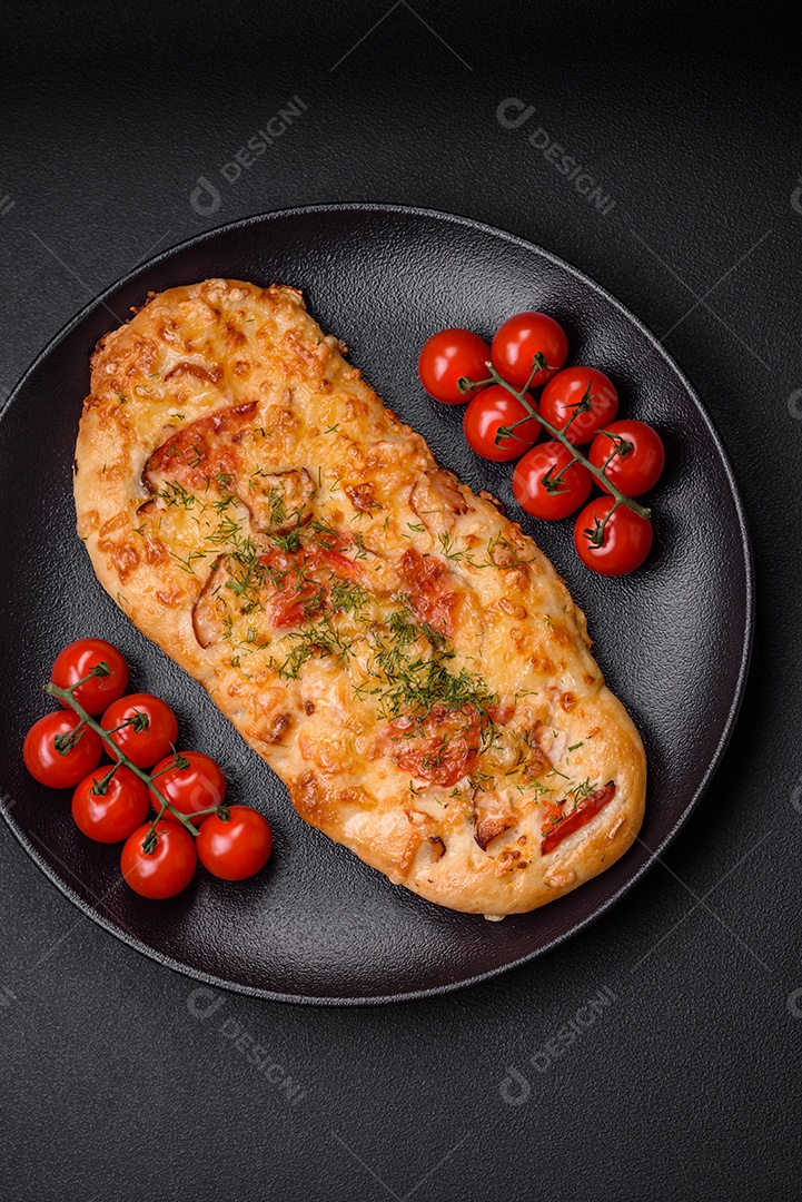 Deliciosa pizza de pão achatado fresco com queijo, tomate, salsicha, sal e especiarias sobre um fundo escuro de concreto