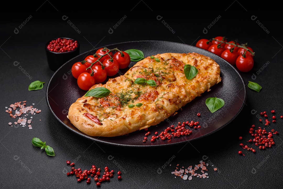 Deliciosa pizza de pão achatado fresco com queijo, tomate, salsicha, sal e especiarias sobre um fundo escuro de concreto
