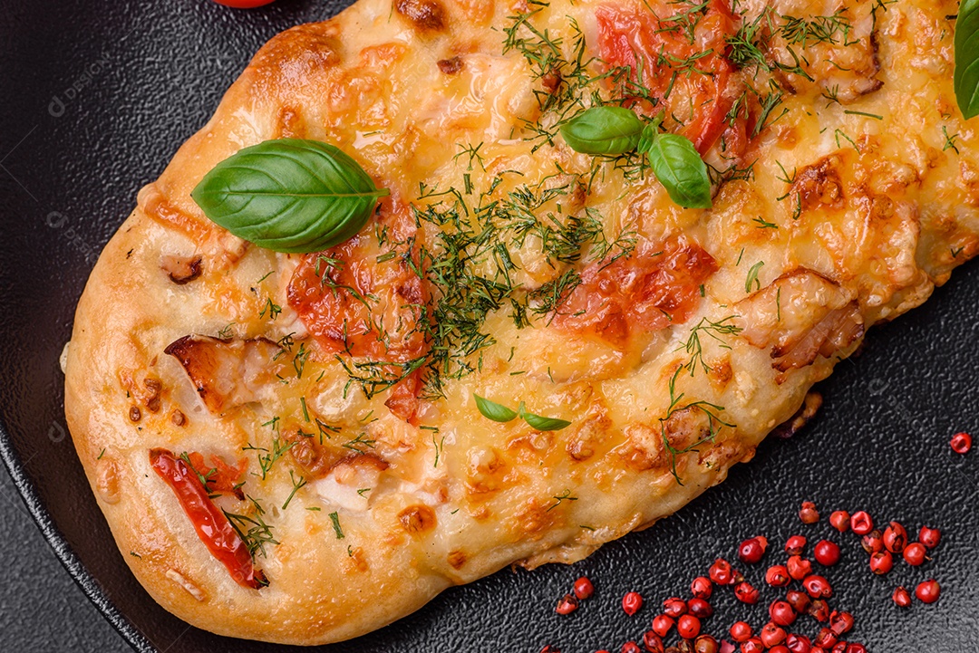 Deliciosa pizza de pão achatado fresco com queijo, tomate, salsicha, sal e especiarias sobre um fundo escuro de concreto