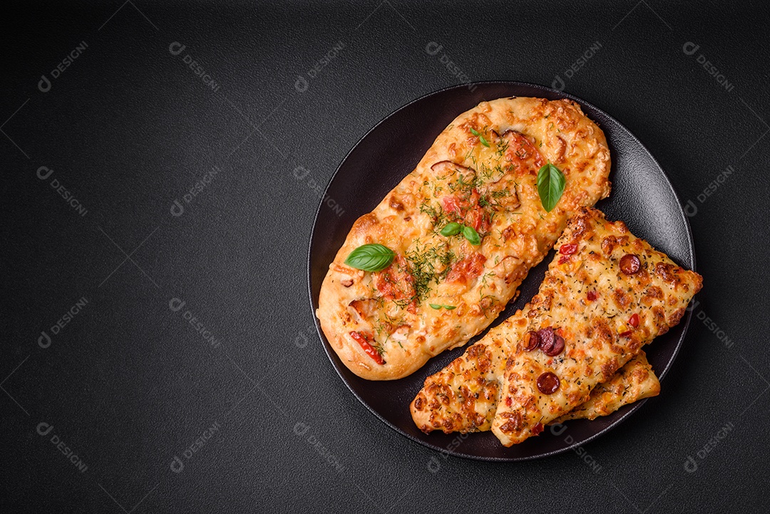 Deliciosa pizza de pão achatado fresco com queijo, tomate, salsicha, sal e especiarias sobre um fundo escuro de concreto