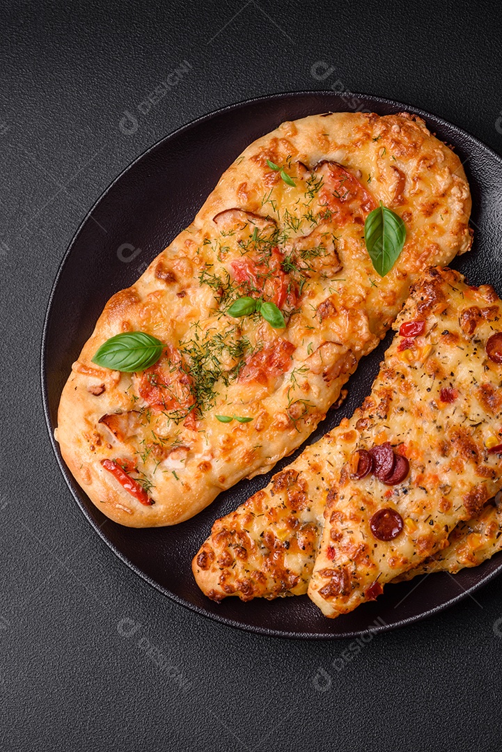 Deliciosa pizza de pão achatado fresco com queijo, tomate, salsicha, sal e especiarias sobre um fundo escuro de concreto