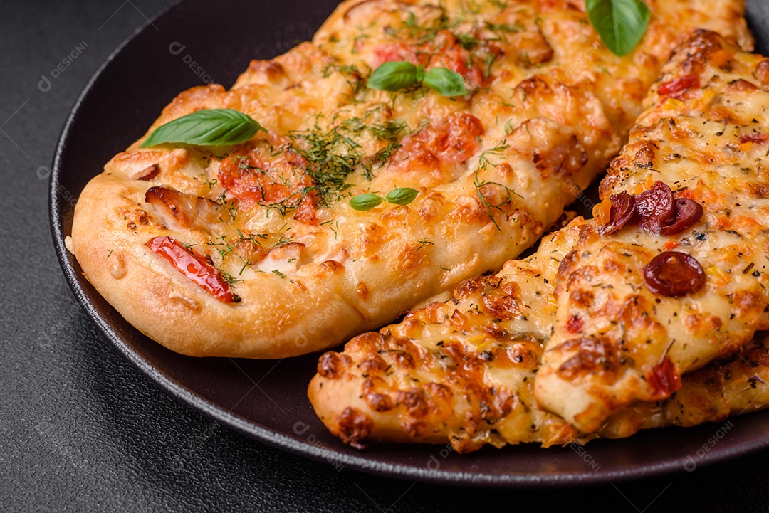 Deliciosa pizza de pão achatado fresco com queijo, tomate, salsicha, sal e especiarias sobre um fundo escuro de concreto