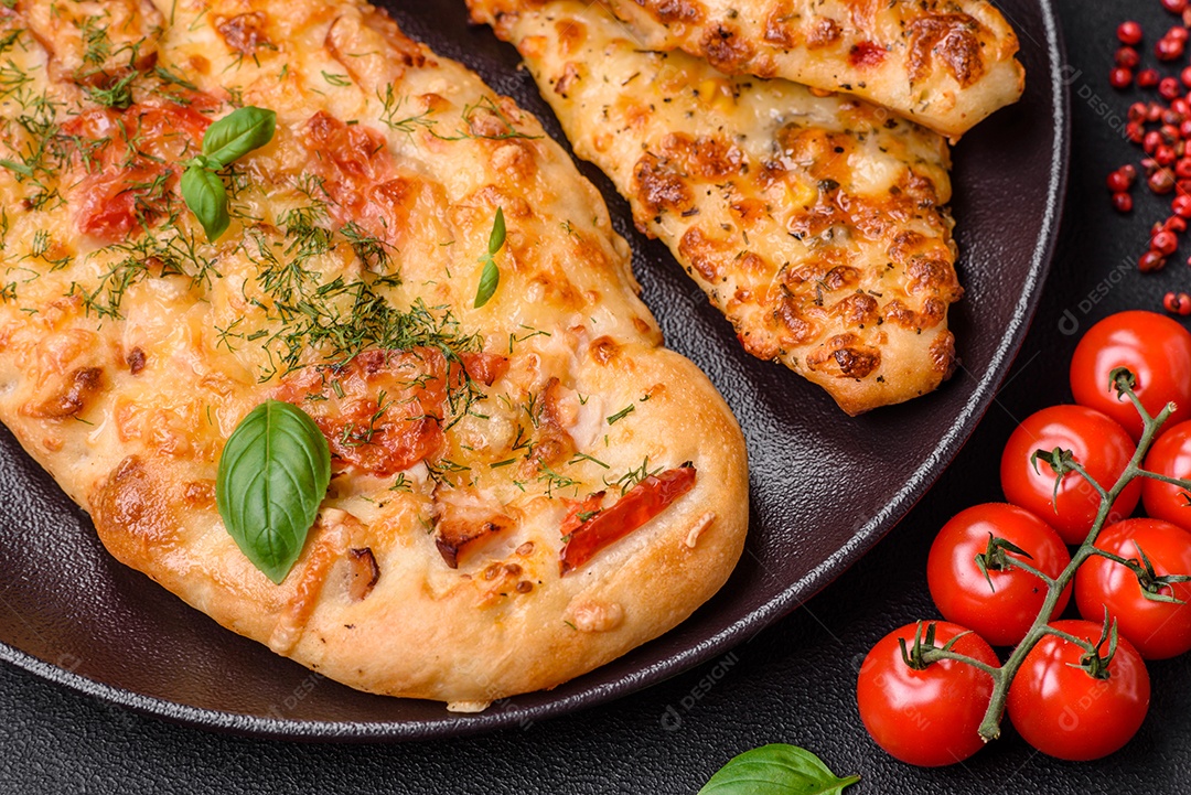 Deliciosa pizza de pão achatado fresco com queijo, tomate, salsicha, sal e especiarias sobre um fundo escuro de concreto