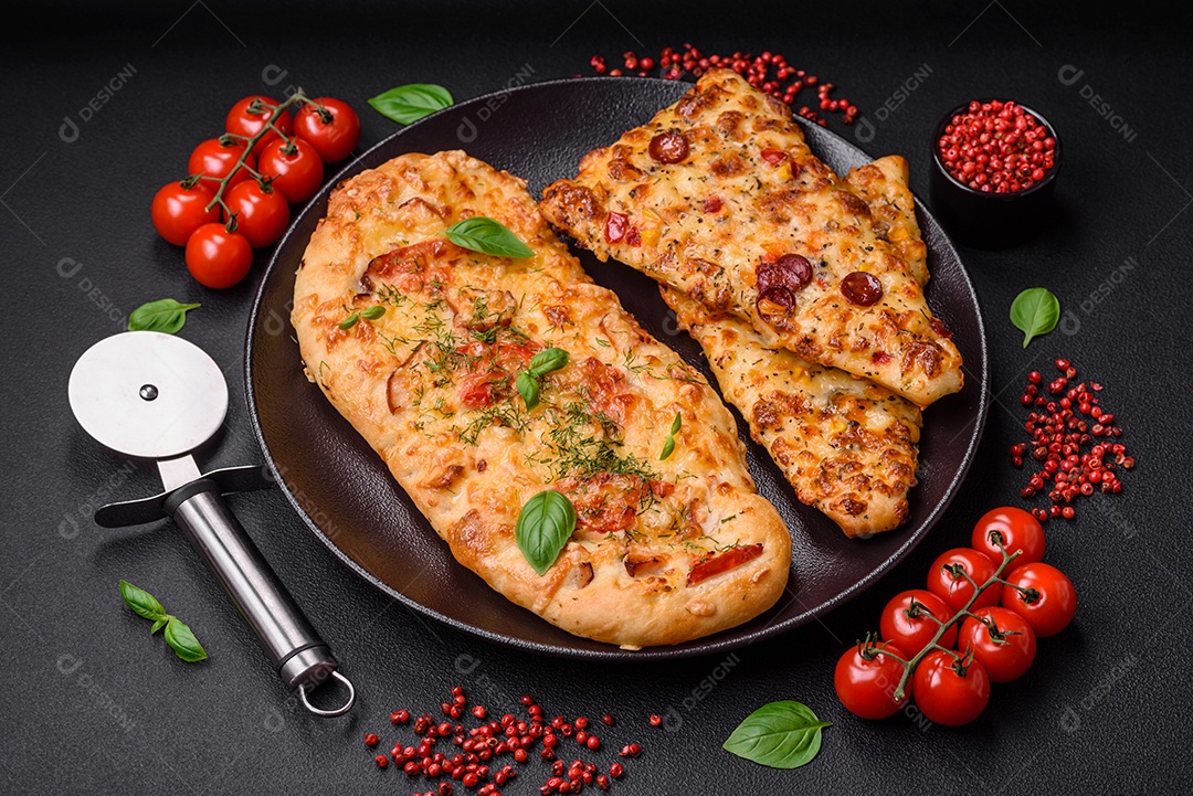 Deliciosa pizza de pão achatado fresco com queijo, tomate, salsicha, sal e especiarias sobre um fundo escuro de concreto