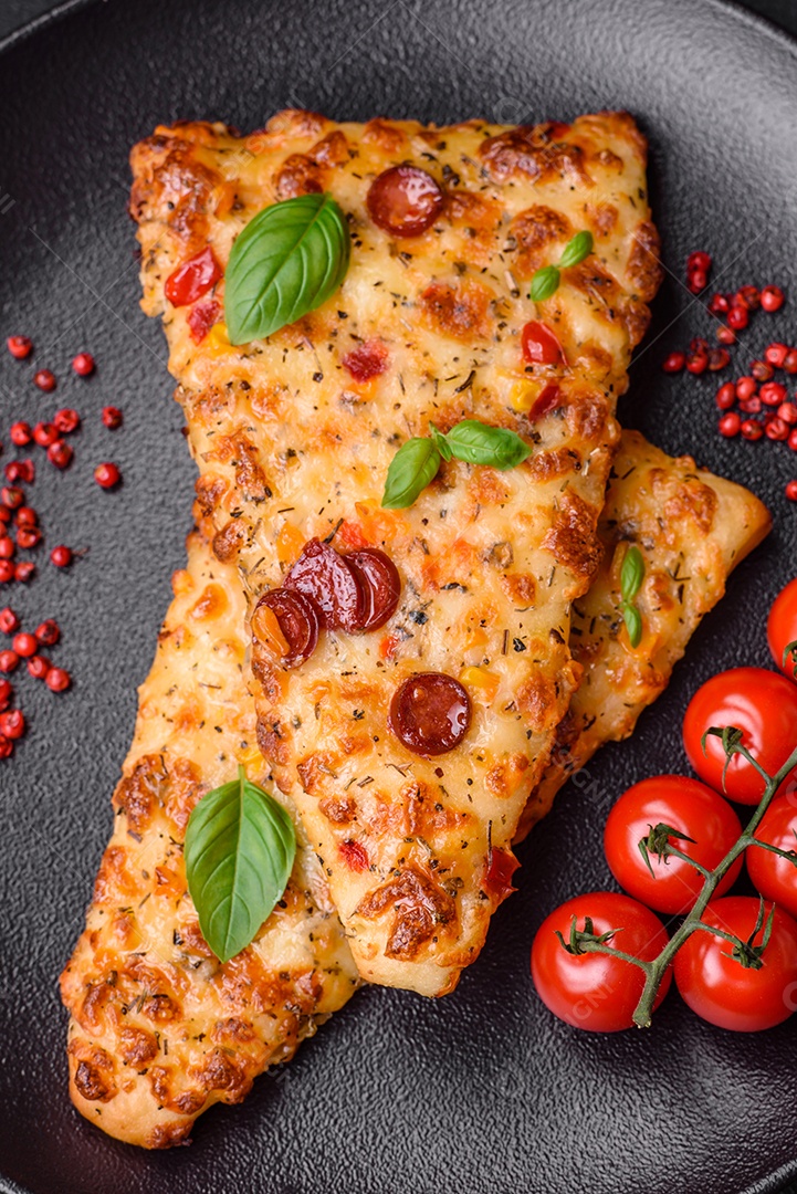 Deliciosa pizza de pão achatado fresco com queijo, tomate, salsicha, sal e especiarias sobre um fundo escuro de concreto