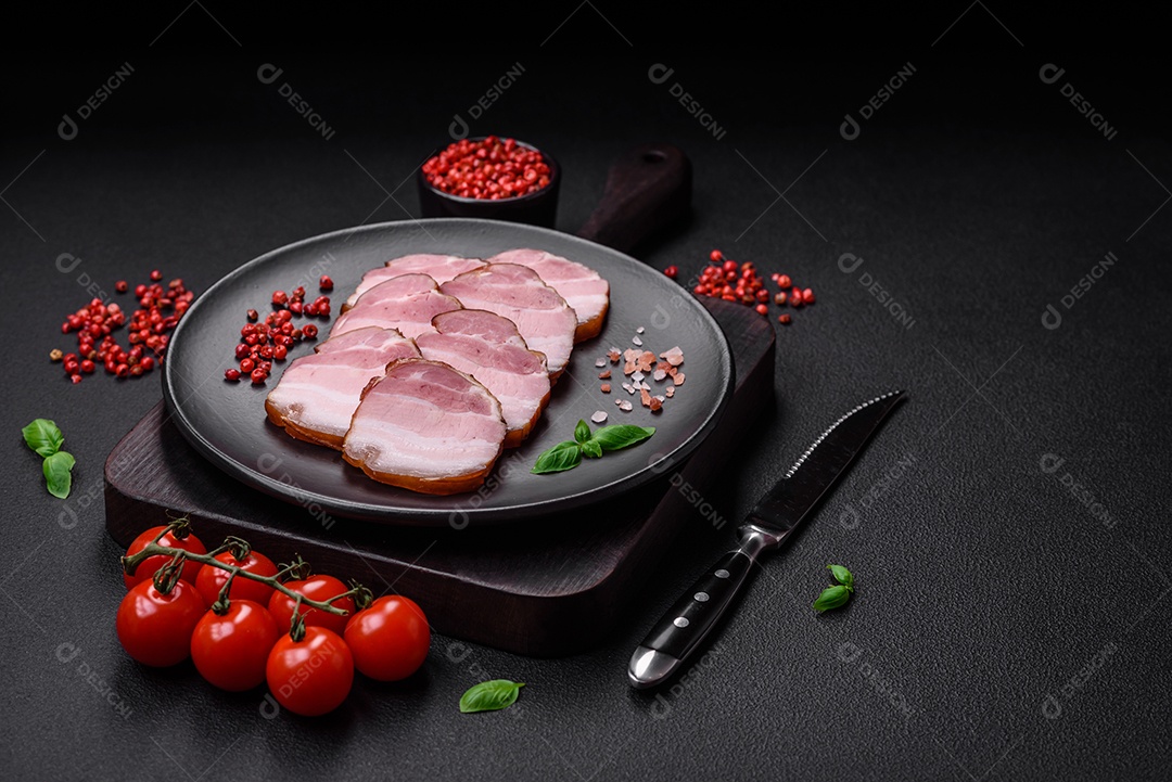 Delicioso bacon defumado com sal, especiarias e ervas sobre um fundo escuro de concreto