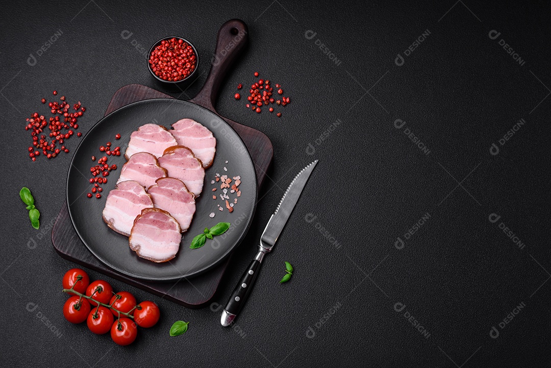 Delicioso bacon defumado com sal, especiarias e ervas sobre um fundo escuro de concreto