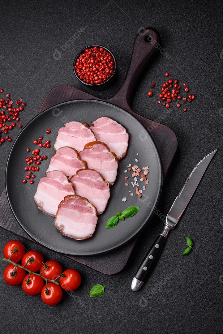 Delicioso bacon defumado com sal, especiarias e ervas sobre um fundo escuro de concreto