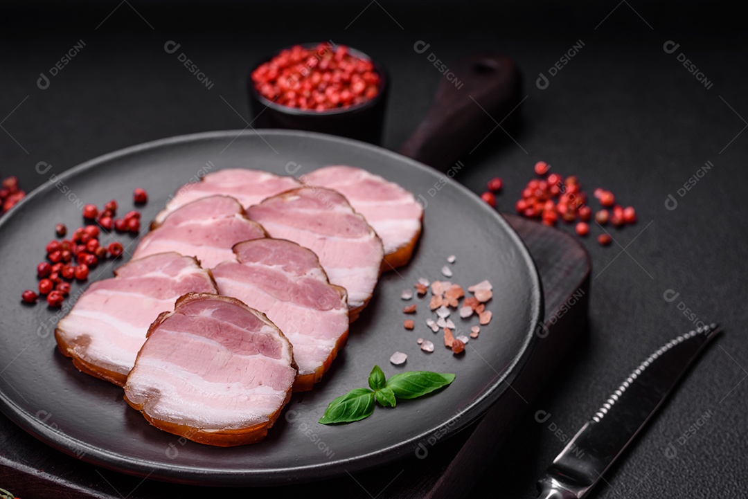 Delicioso bacon defumado com sal, especiarias e ervas sobre um fundo escuro de concreto