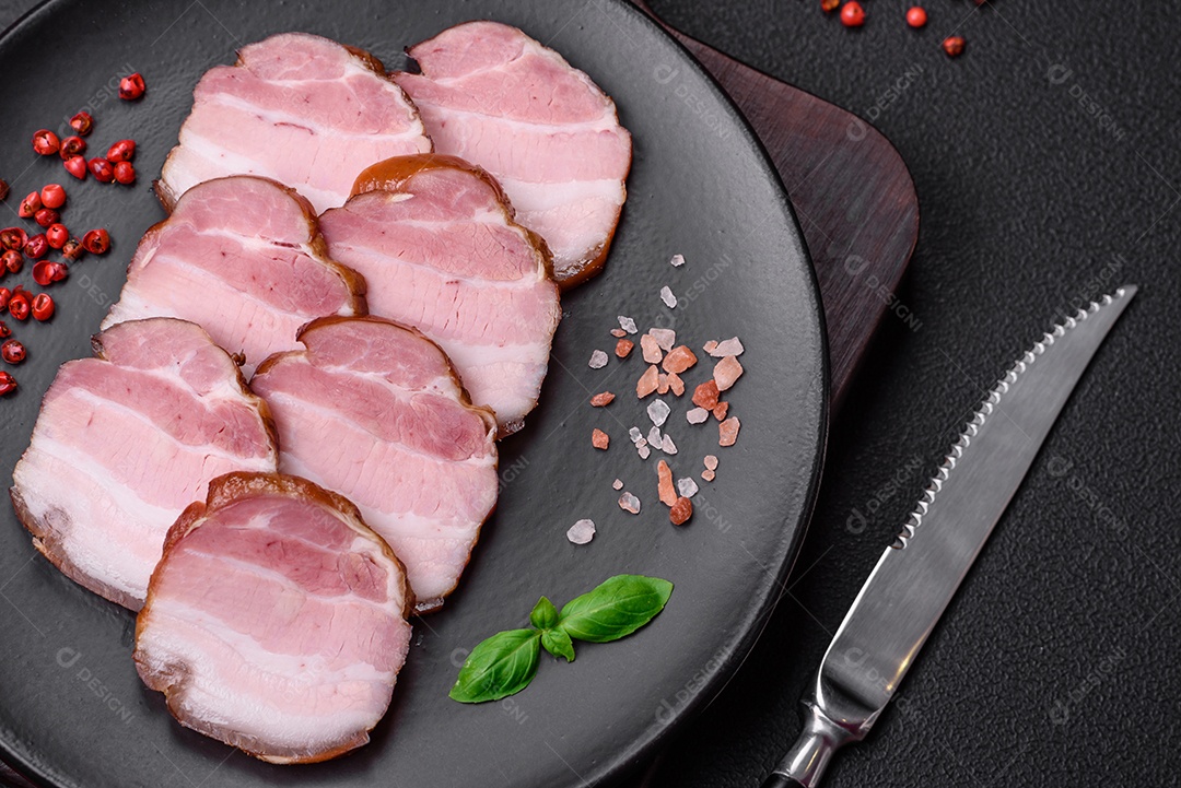 Delicioso bacon defumado com sal, especiarias e ervas sobre um fundo escuro de concreto