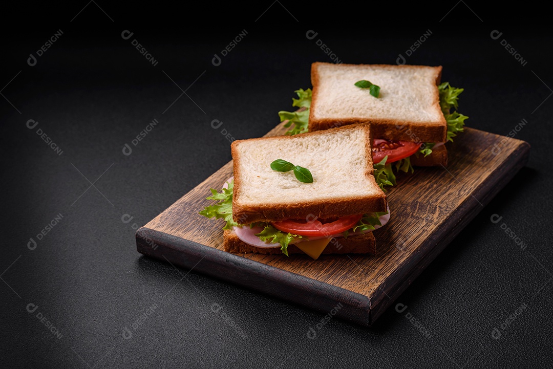 Delicioso sanduíche com torradas, presunto, tomate, queijo e alface com sal, especiarias e ervas sobre fundo escuro de concreto