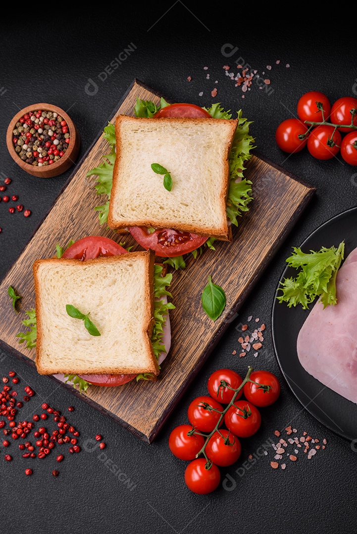 Delicioso sanduíche com torradas, presunto, tomate, queijo e alface com sal, especiarias e ervas sobre fundo escuro de concreto