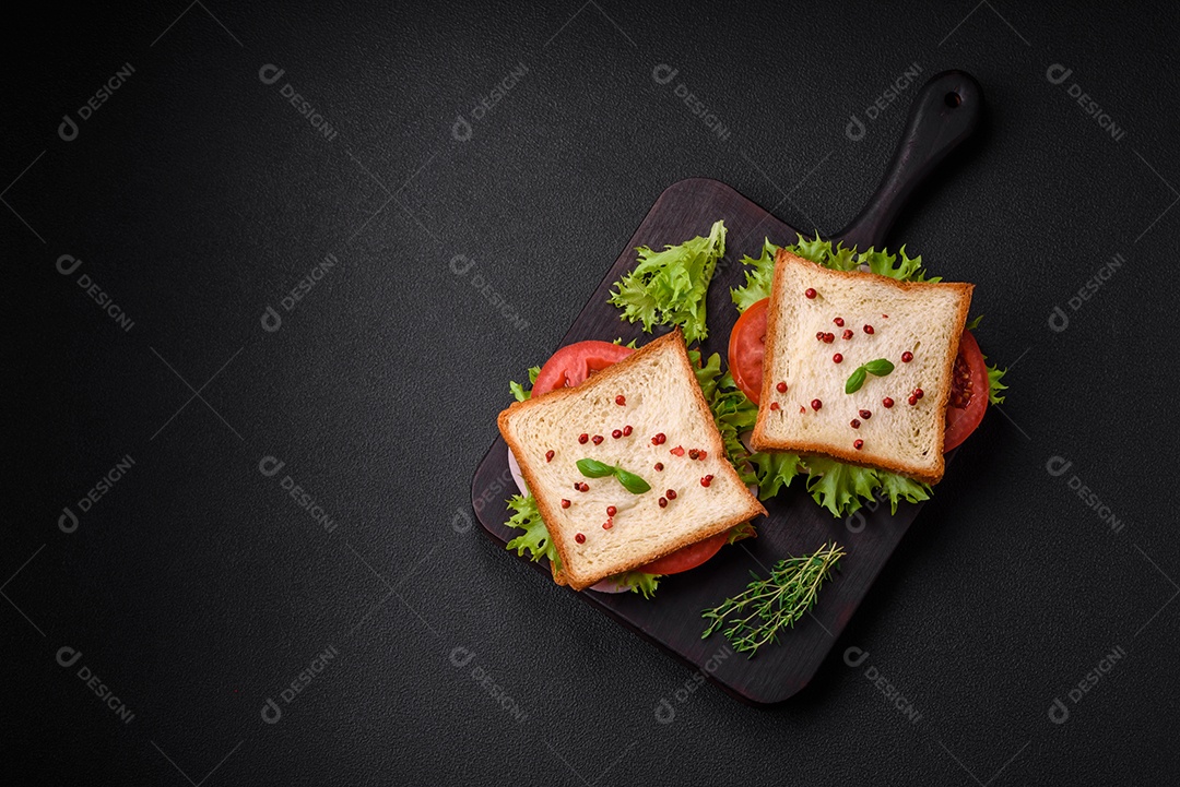 Delicioso sanduíche com torradas, presunto, tomate, queijo e alface com sal, especiarias e ervas sobre fundo escuro de concreto