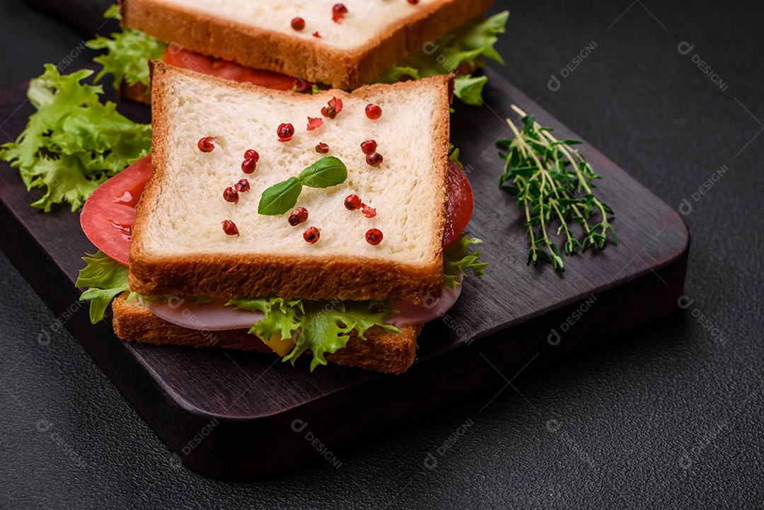 Delicioso sanduíche com torradas, presunto, tomate, queijo e alface com sal, especiarias e ervas sobre fundo escuro de concreto