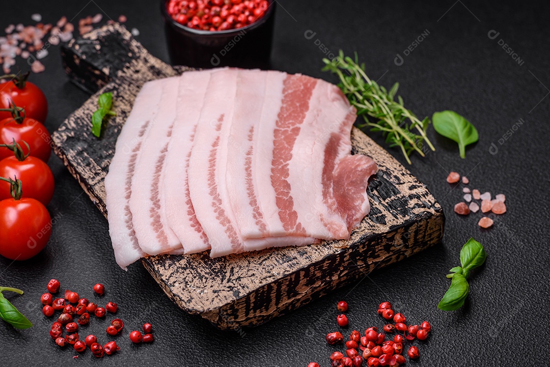 Bacon cru fresco cortado em fatias com sal, especiarias e ervas sobre um fundo de concreto texturizado escuro