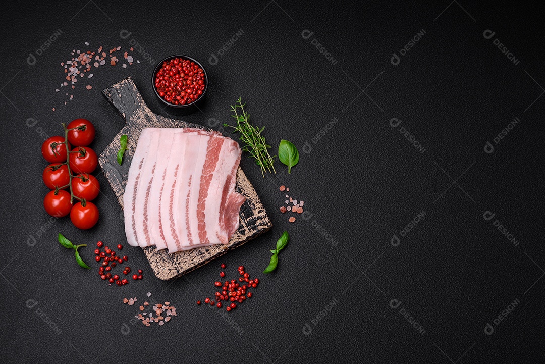 Bacon cru fresco cortado em fatias com sal, especiarias e ervas sobre um fundo de concreto texturizado escuro