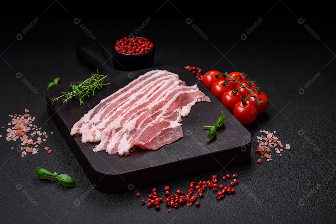 Bacon cru fresco cortado em fatias com sal, especiarias e ervas sobre um fundo de concreto texturizado escuro