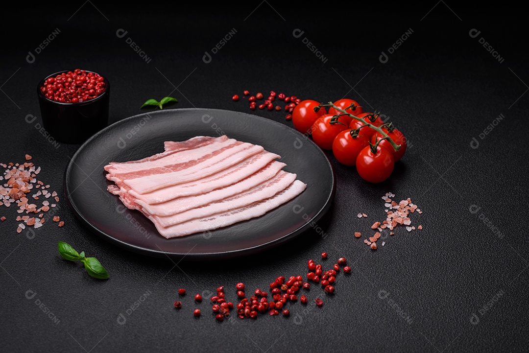 Bacon cru fresco cortado em fatias com sal, especiarias e ervas sobre um fundo de concreto texturizado escuro