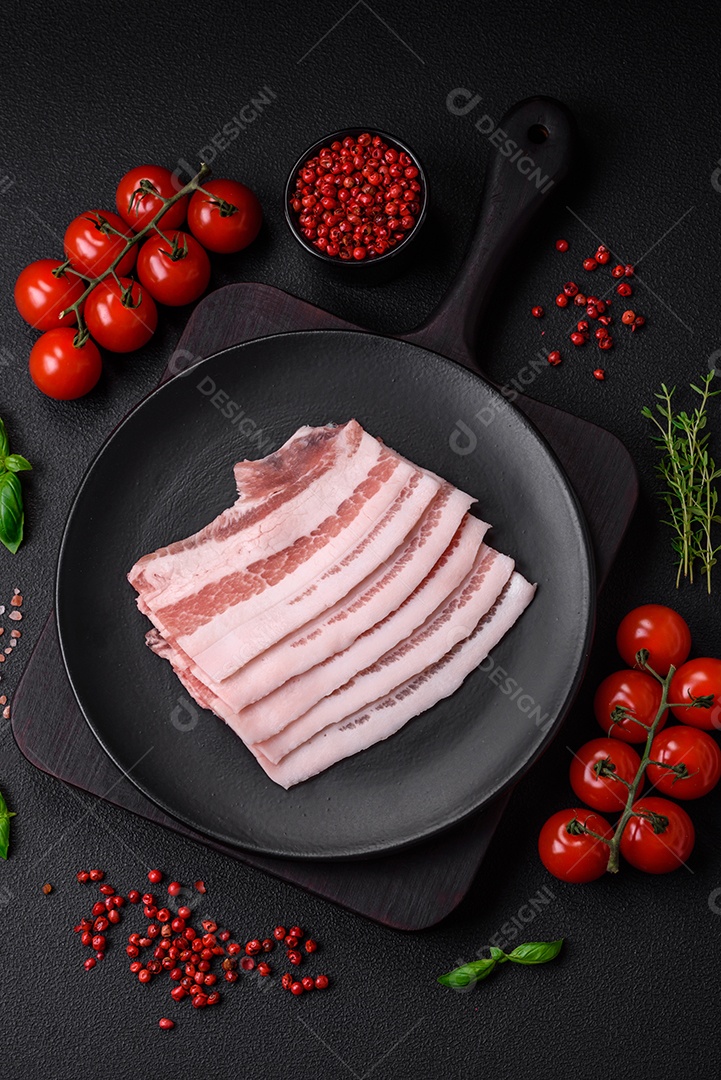 Bacon cru fresco cortado em fatias com sal, especiarias e ervas sobre um fundo de concreto texturizado escuro