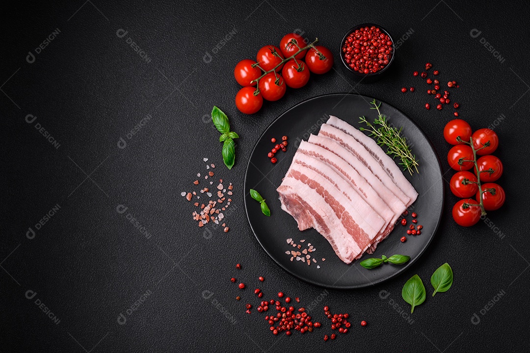 Bacon cru fresco cortado em fatias com sal, especiarias e ervas sobre um fundo de concreto texturizado escuro