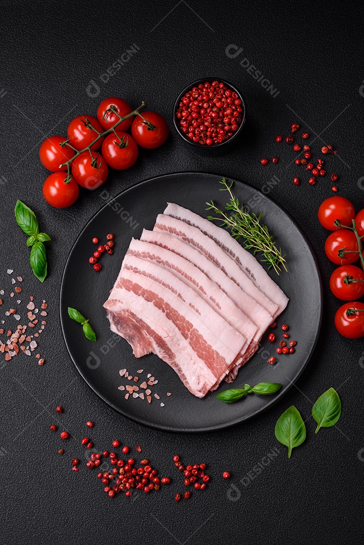 Bacon cru fresco cortado em fatias com sal, especiarias e ervas sobre um fundo de concreto texturizado escuro