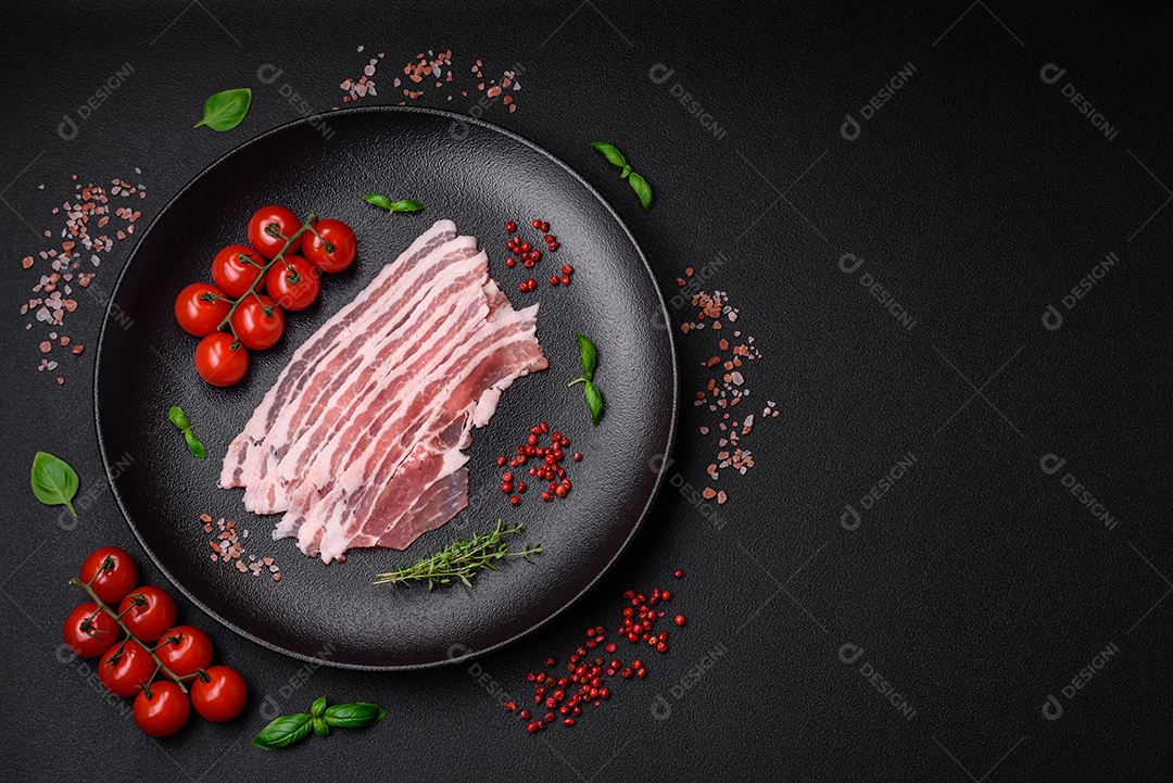 Bacon cru fresco cortado em fatias com sal, especiarias e ervas sobre um fundo de concreto texturizado escuro